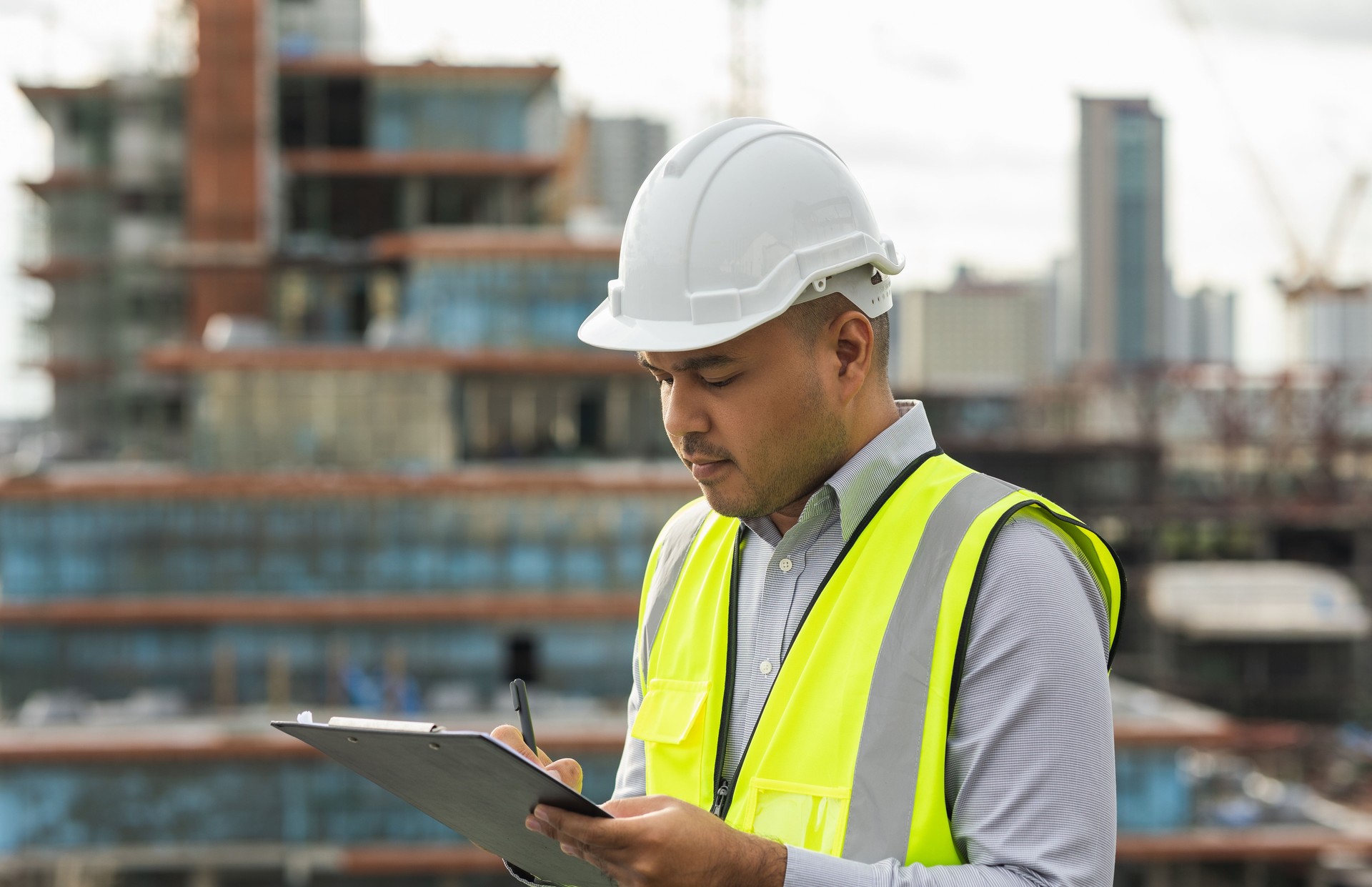 Inspector engineer man or architect with clipboard with white safety helmet in city construction site. Checking with checklist on rooftop building construction at capital.